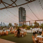 Elegant rooftop event with tables and lights set against Mumbai skyline at sunset, India.
